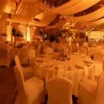 Elegantna dvorana za događanja s ukrašenim stolovima i svjetlosnim ukrasima.