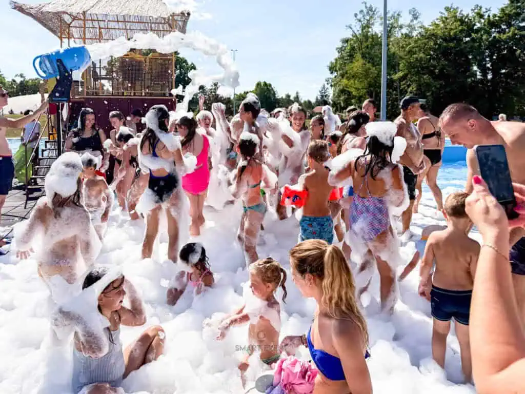 Pjena na zabavi s mnoštvom ljudi, djece i odraslih, uživajući u zabavi s pjenom na otvorenom prostor.